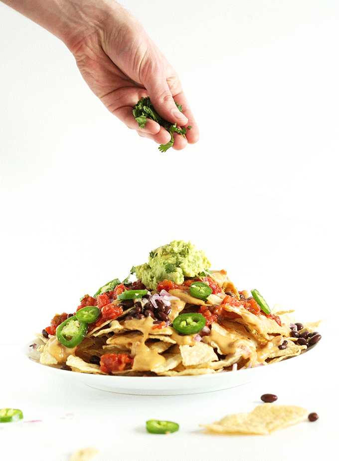 Sprinkling cilantro onto a plate of The Best Damn Vegan Nachos