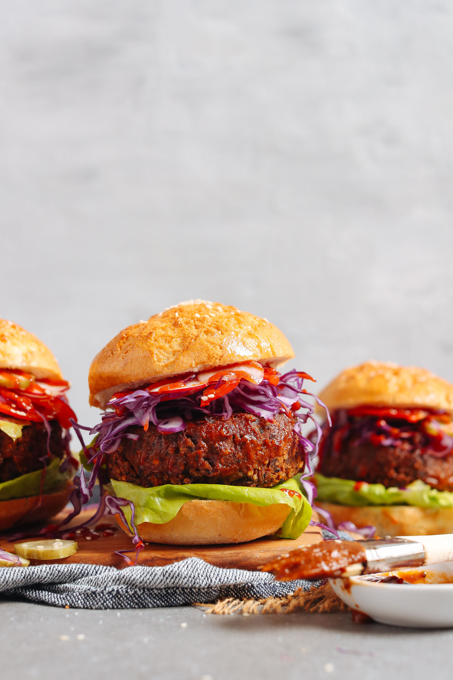 Three BBQ Black Bean Burgers served on buns with red bell pepper, cabbage, and lettuce