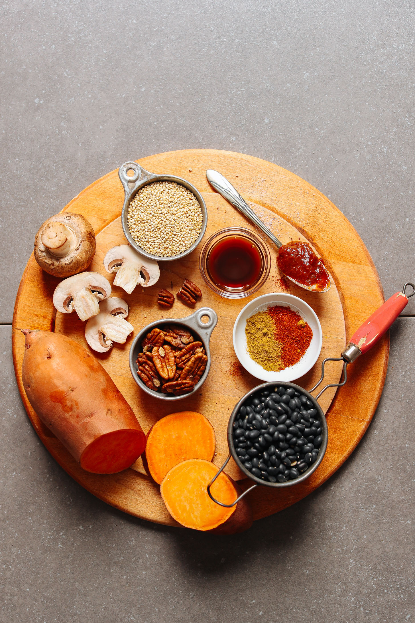 Display of ingredients for vegan BBQ Black Bean Burgers including mushrooms, sweet potato, pecans, black beans, BBQ sauce, coconut aminos, spices, and quinoa