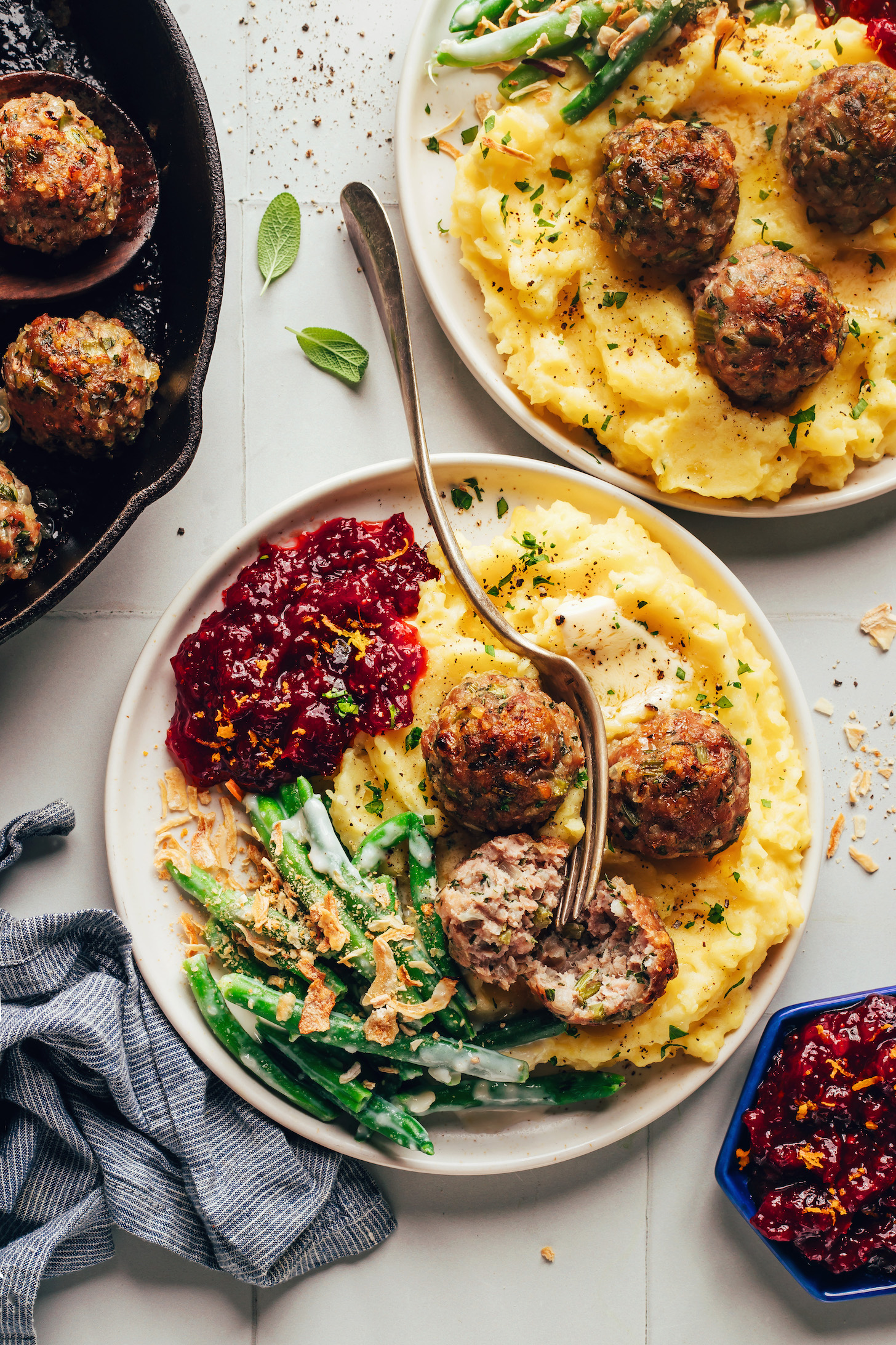 Plates filled with a Thanksgiving feast of turkey meatballs, mashed potatoes, green bean casserole, and cranberry sauce