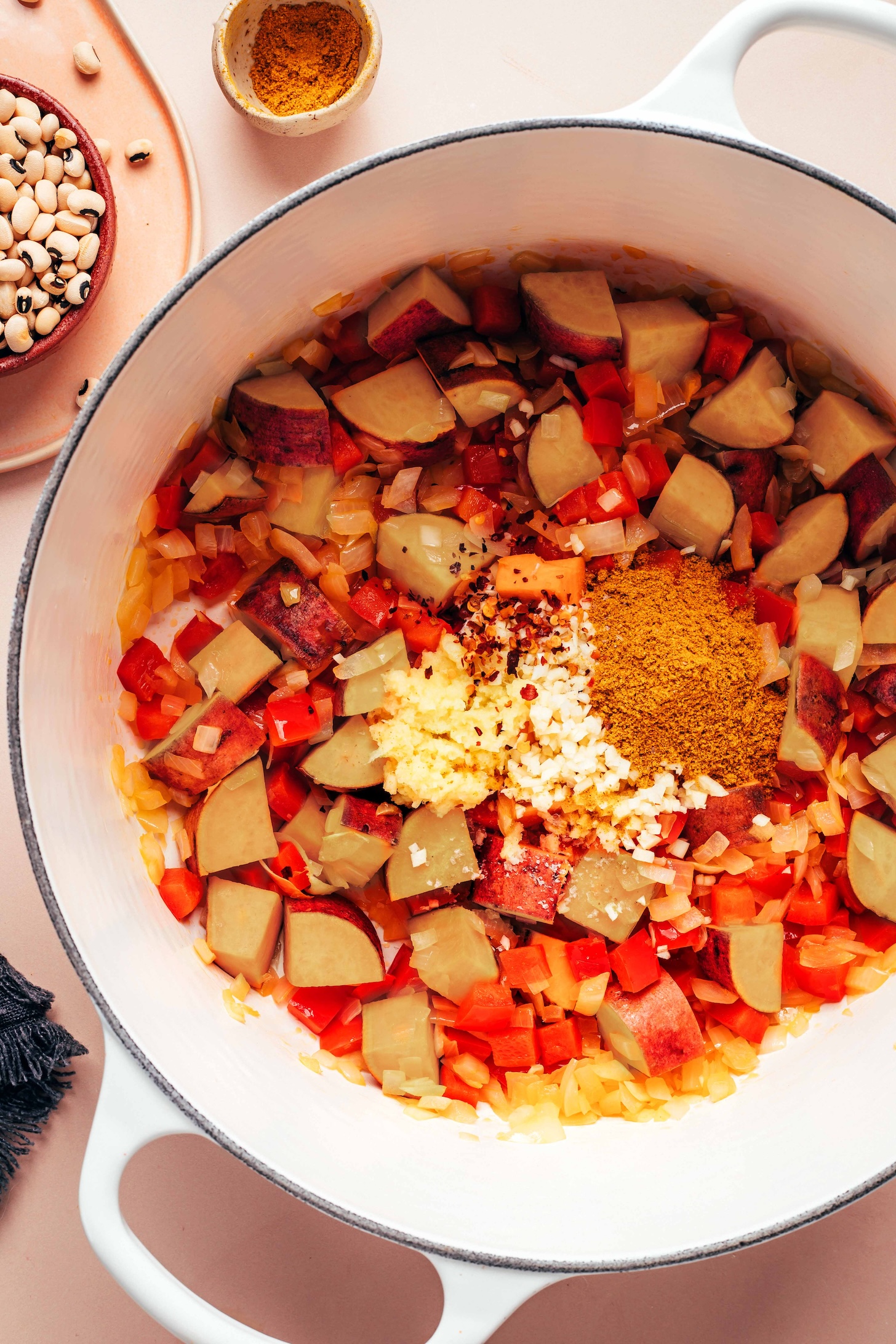 Dutch oven with sautéed onion, bell pepper, and sweet potato topped with garlic, ginger, red pepper flakes, and curry powder