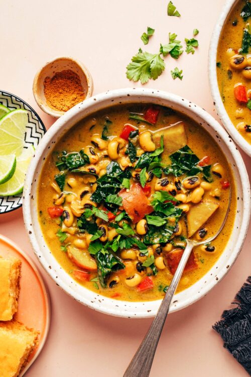 Overhead photo of a bowl of creamy curried black eyed pea soup next to ingredients used to make it and cornbread for serving