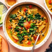 Close up photo of a bowl of curried black eyed pea soup with a spoon resting in it