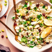Fork and spoon resting in a bowl of our easy raw chopped cauliflower salad