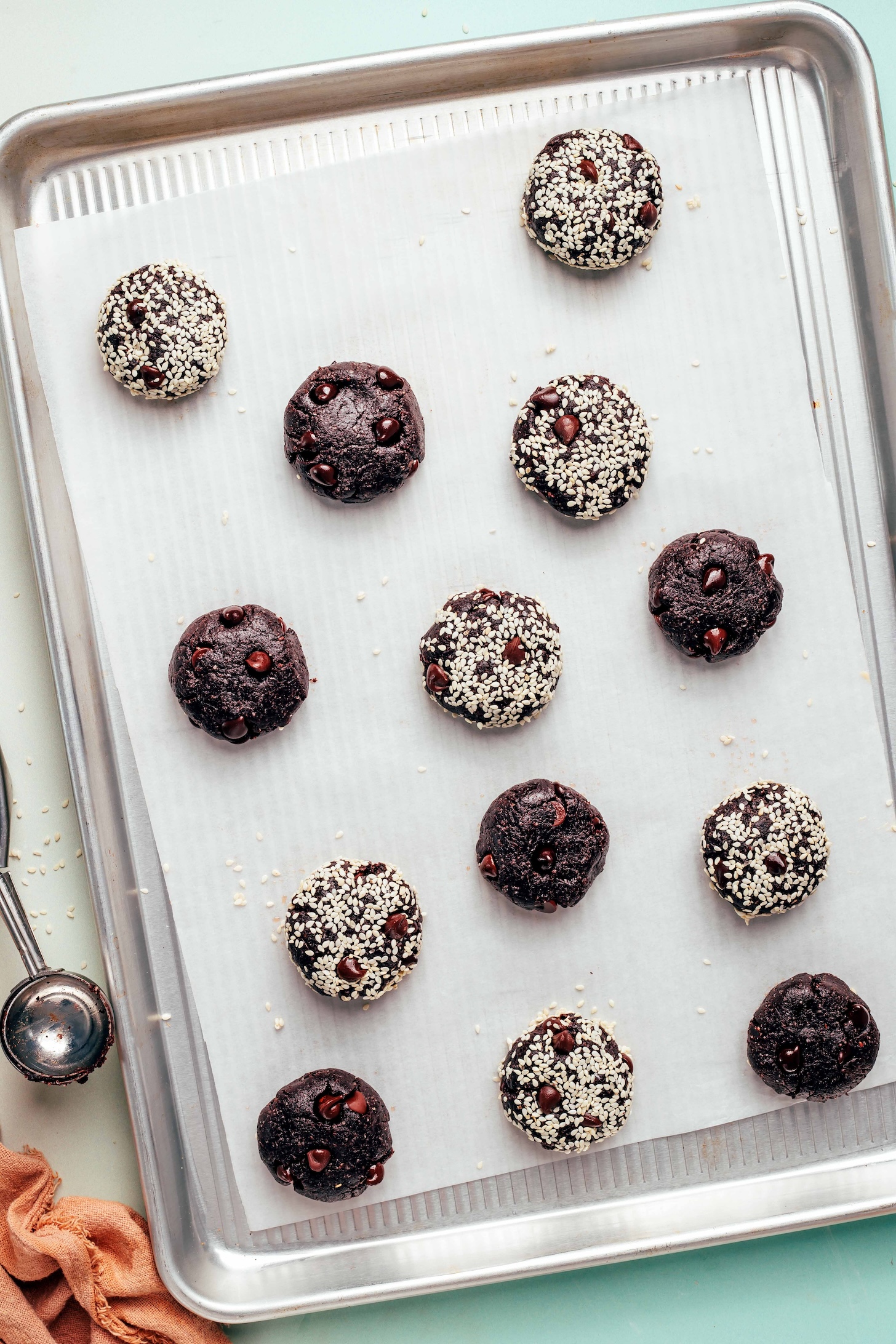 Chocolate tahini cookies on a baking sheet with some plain and some coated in sesame seeds