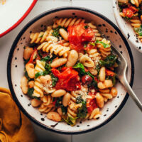 Overhead shot of a bowl of pasta with white beans, cherry tomatoes, olives, and kale