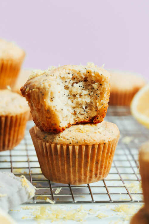Stack of vegan gluten-free lemon poppy seed muffins with the top one partially eaten to show the fluffy inner texture