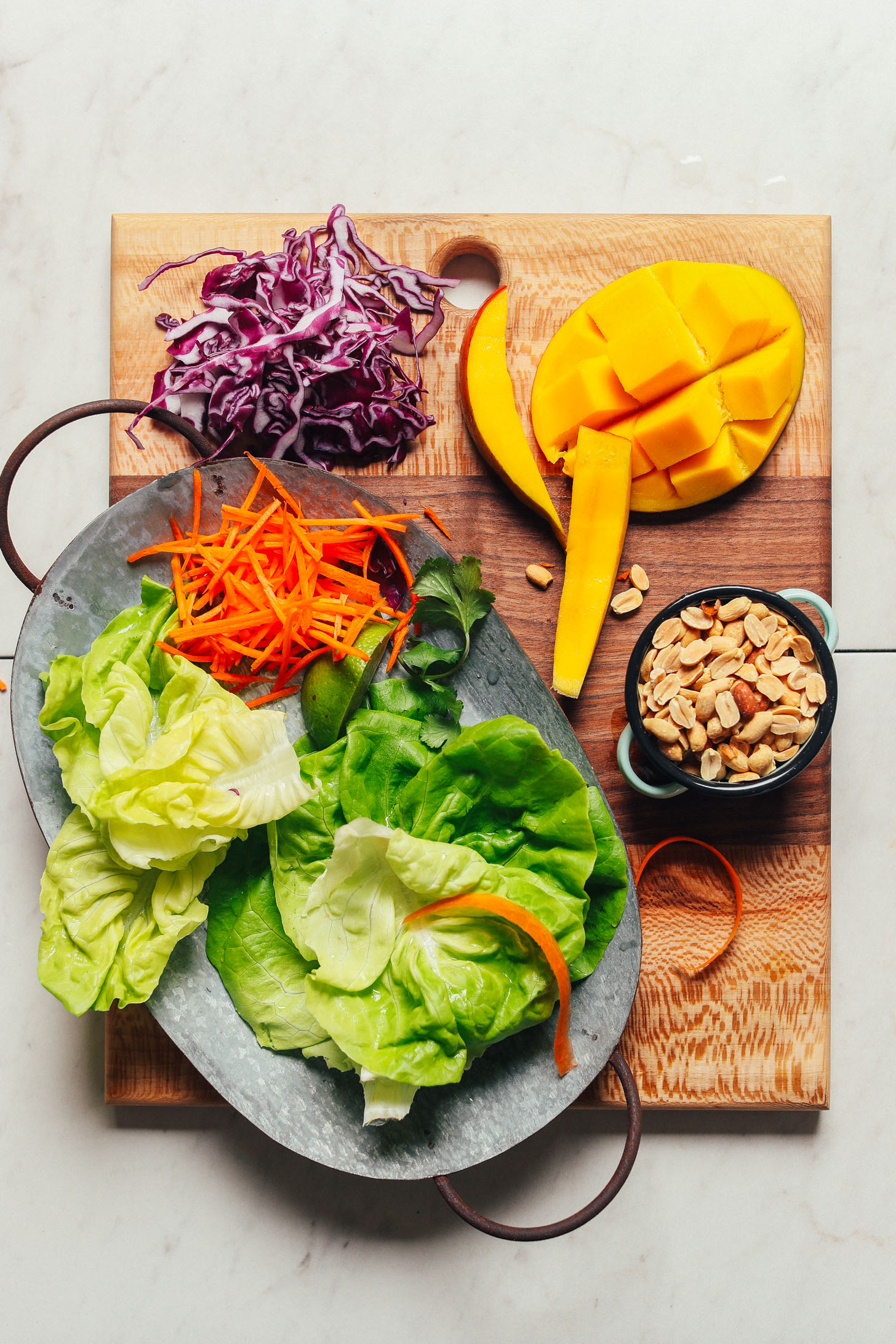 Cutting board with lettuce, carrots, red cabbage, mango, and peanuts for making a healthy vegan salad