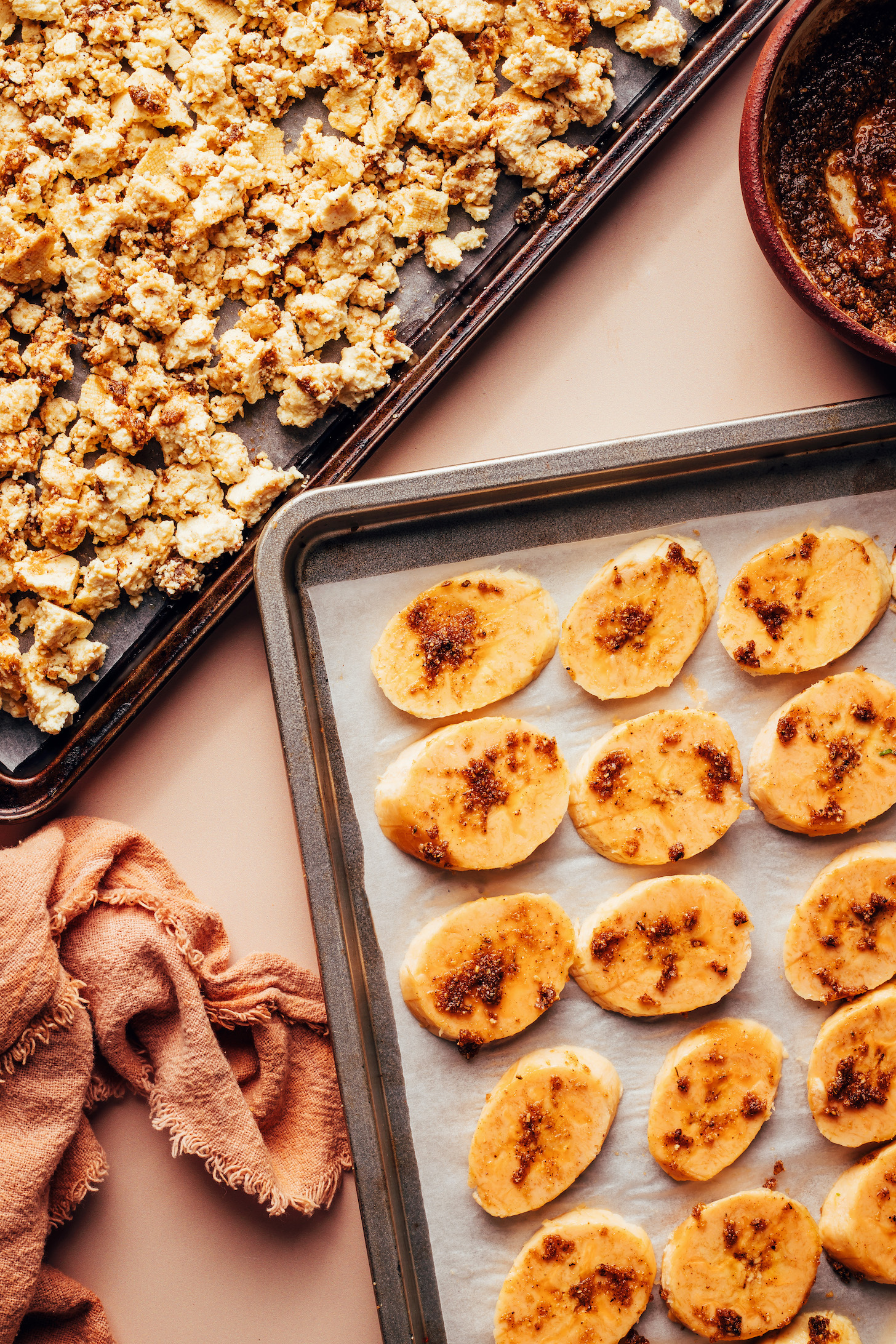 Baking sheets of crumbled tofu and sliced plantains both coated in homemade jerk sauce