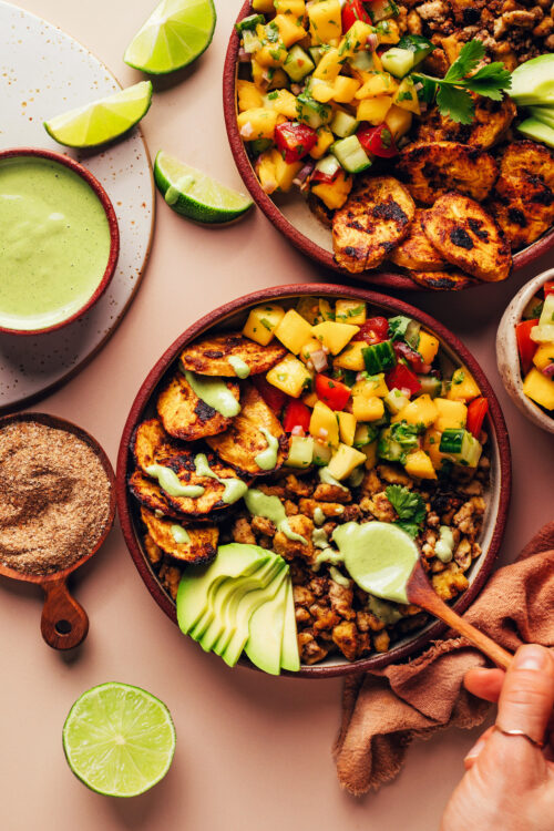 Drizzling a creamy green sauce onto Jerk Tofu & Roasted Plantain Bowls