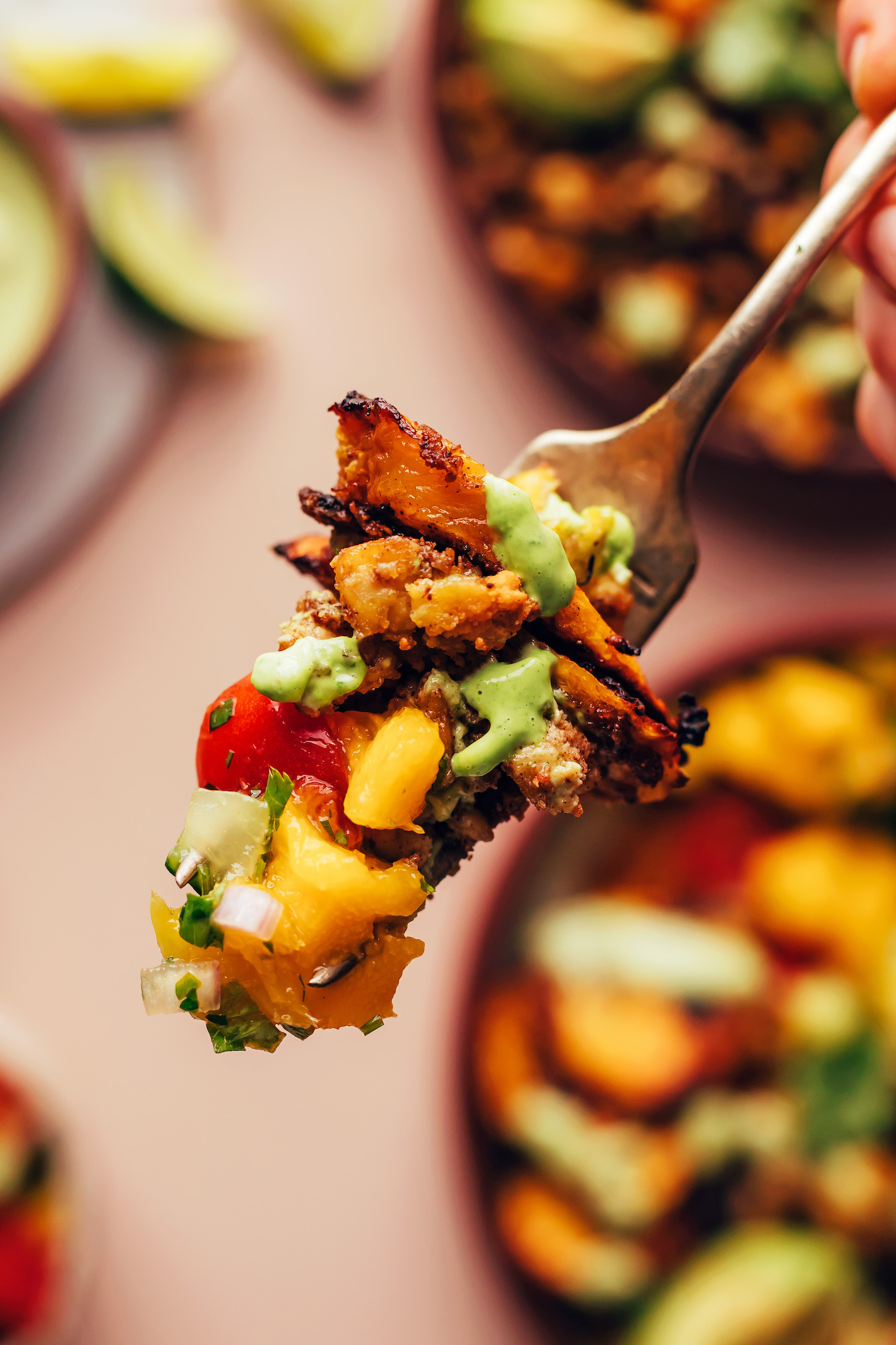 Fork with a bite of jerk tofu, jerk plantains, mango salad, and green tahini sauce