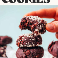 Fingers holding a partially eaten fudgy chocolate tahini cookie above a stack of cookies with text that says made in 1 bowl