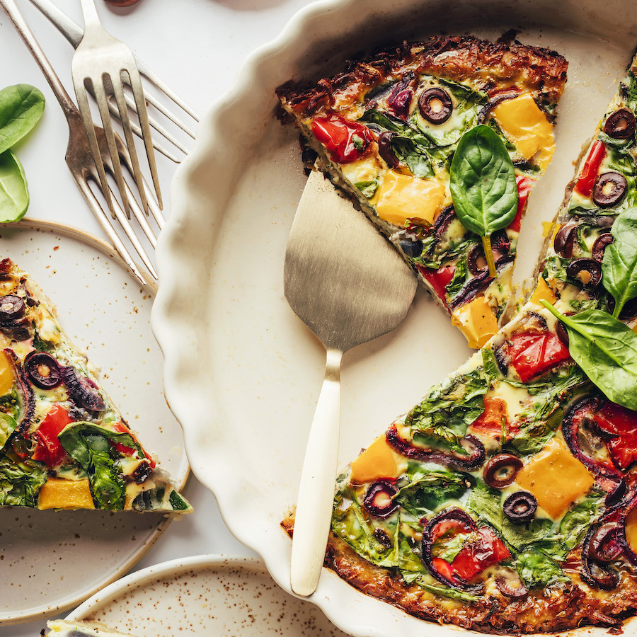 Overhead shot of a partially sliced quiche with veggies