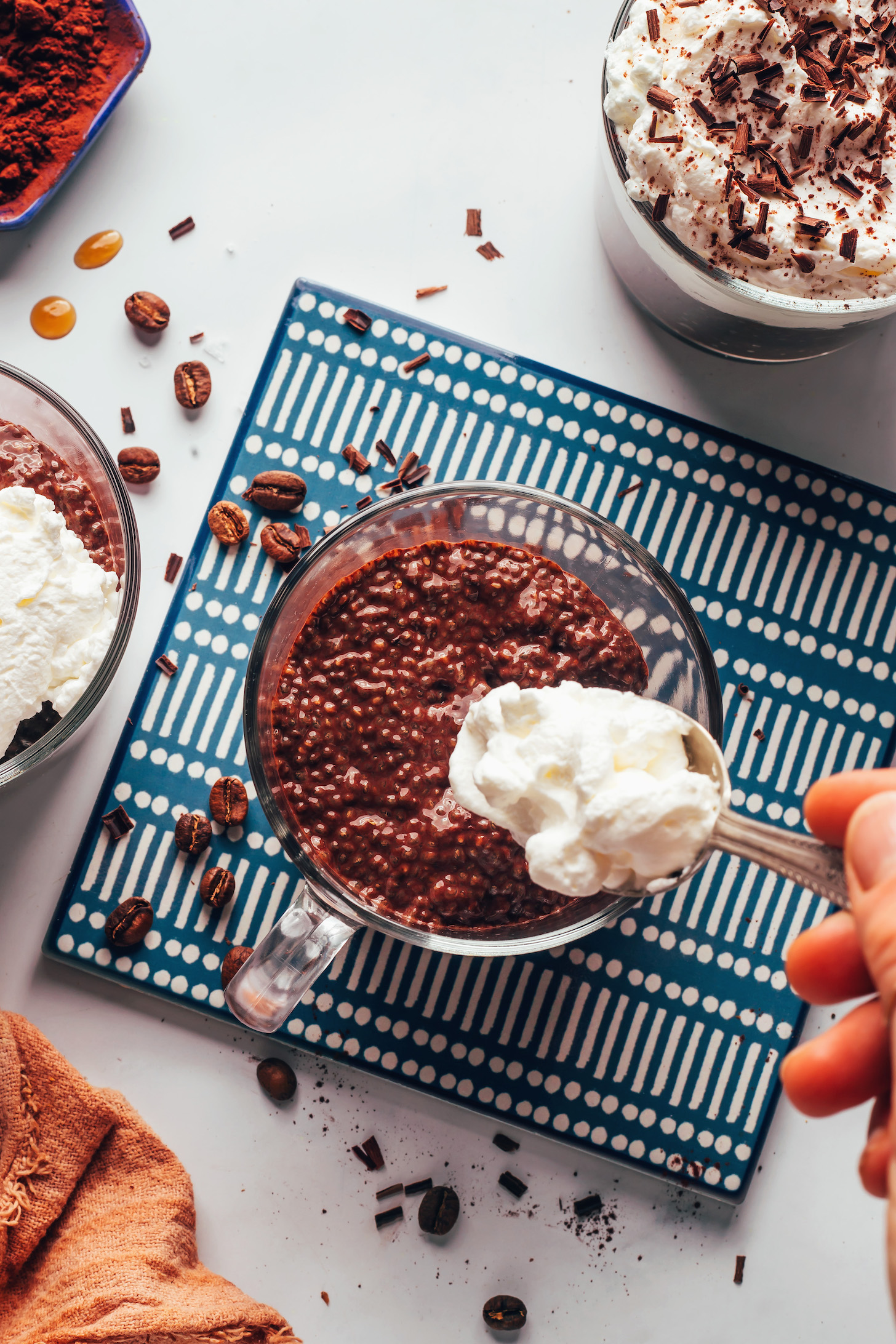 Using a spoon to add coconut whipped cream on top of a mug of chocolate coffee chia pudding