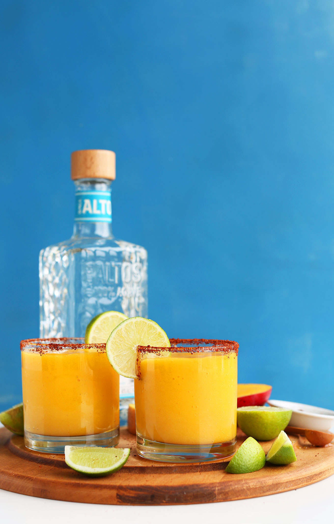 Cutting board with Spicy Sweet Mango Chili Lime Margaritas and ingredients used to make them