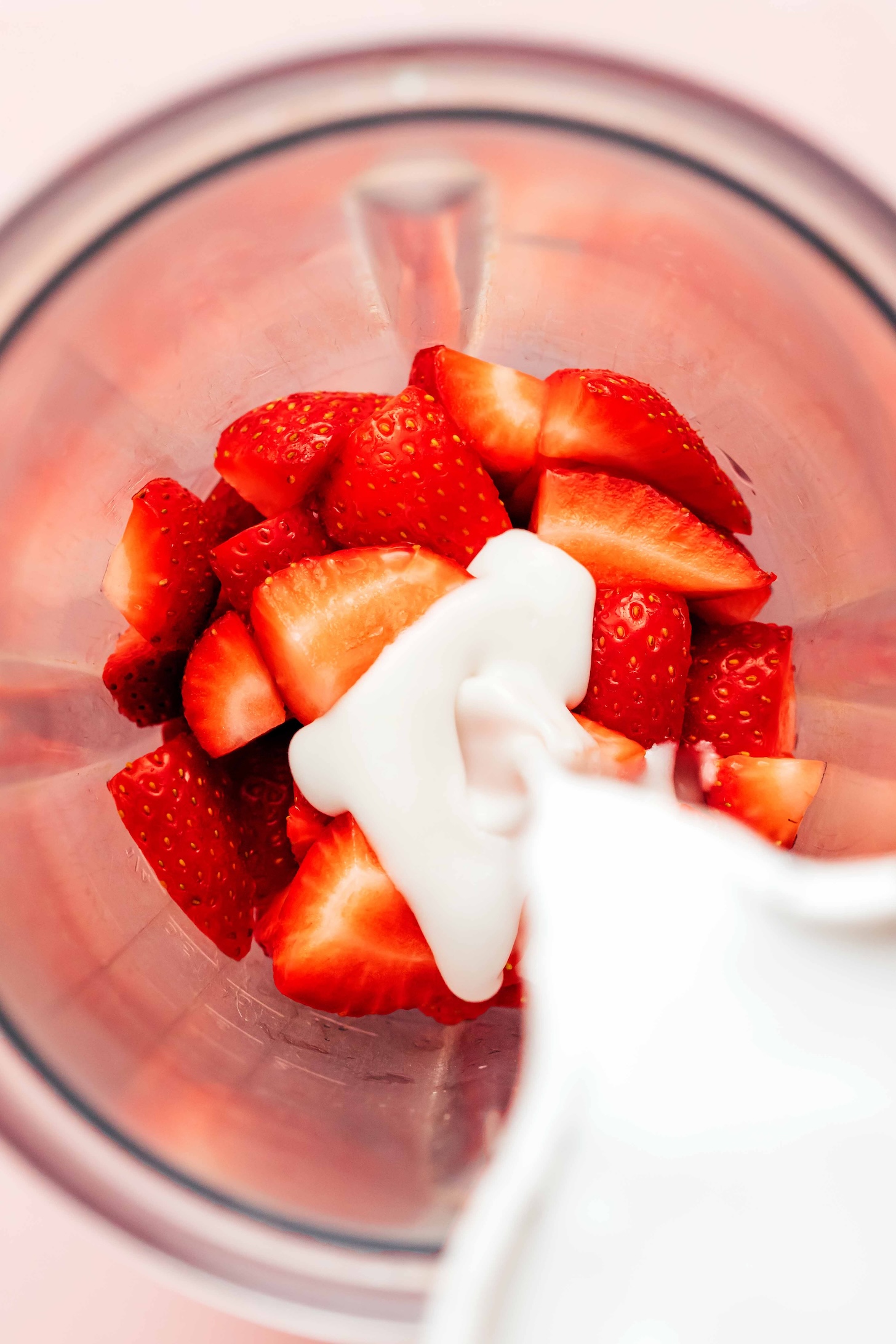 Pouring coconut milk into a blender with fresh chopped strawberries