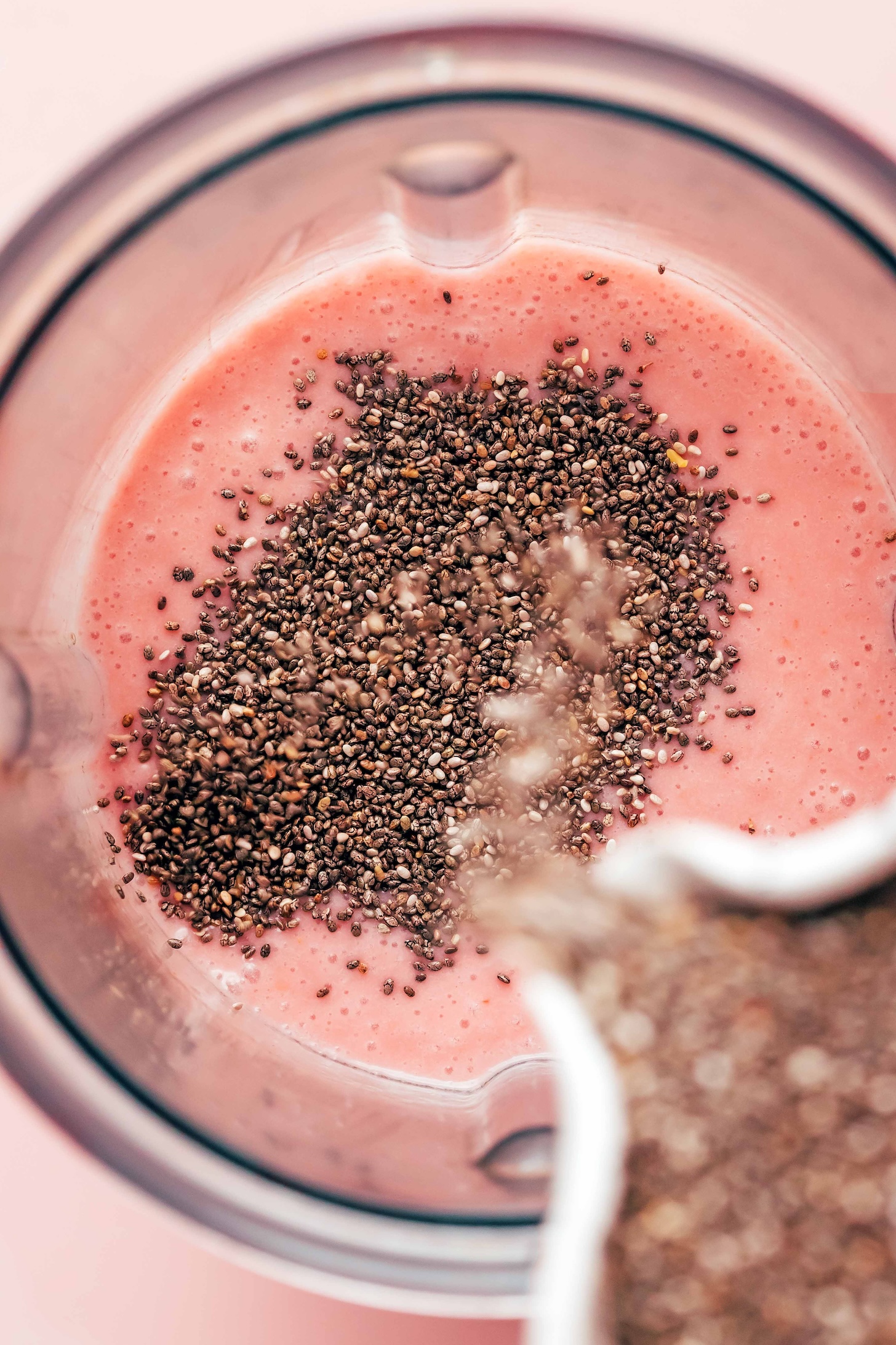 Pouring chia seeds into a blender of strawberry coconut milk