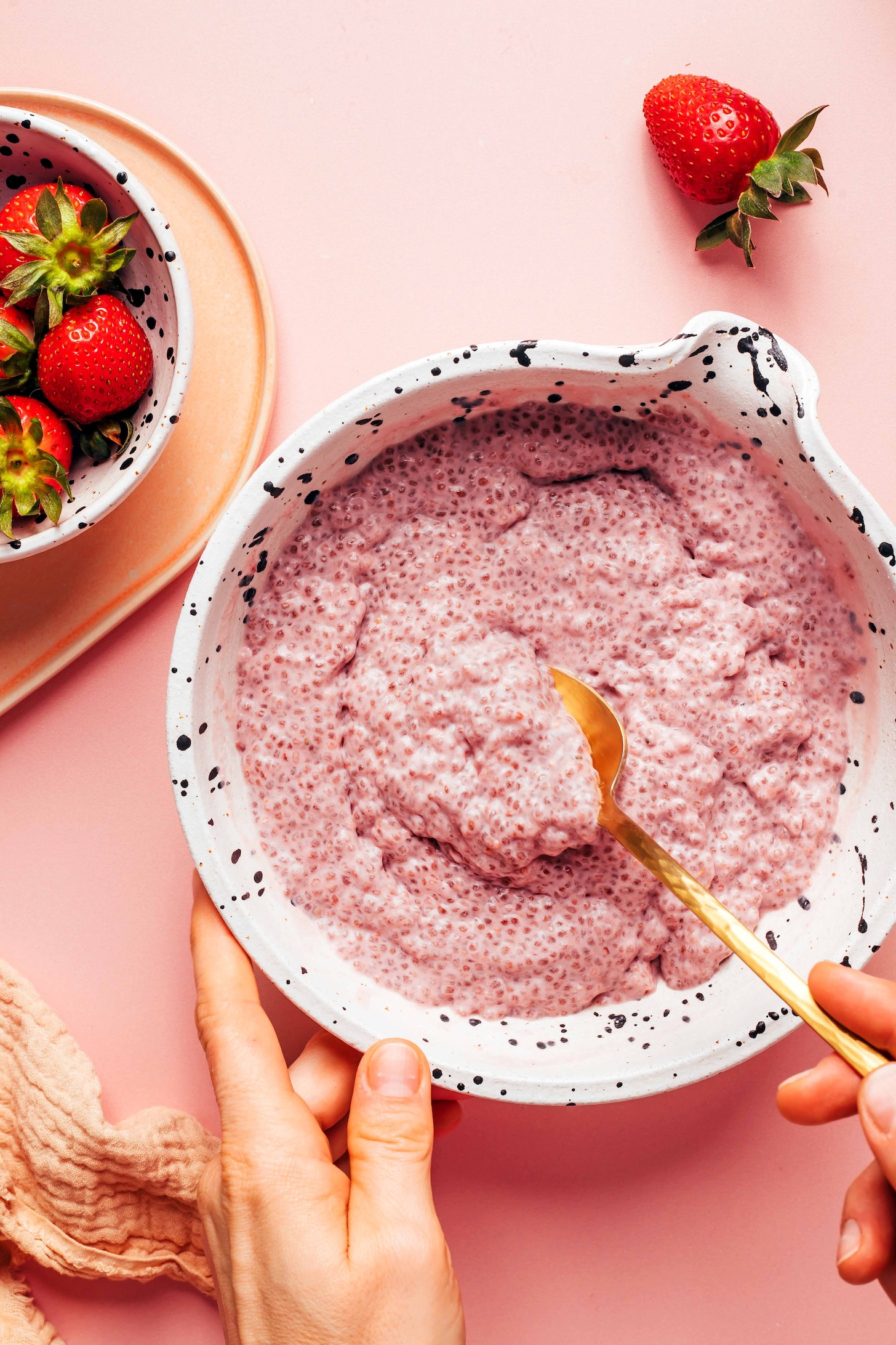 Gold spoon resting in a bowl of strawberry chia pudding next to a bowl of fresh strawberries