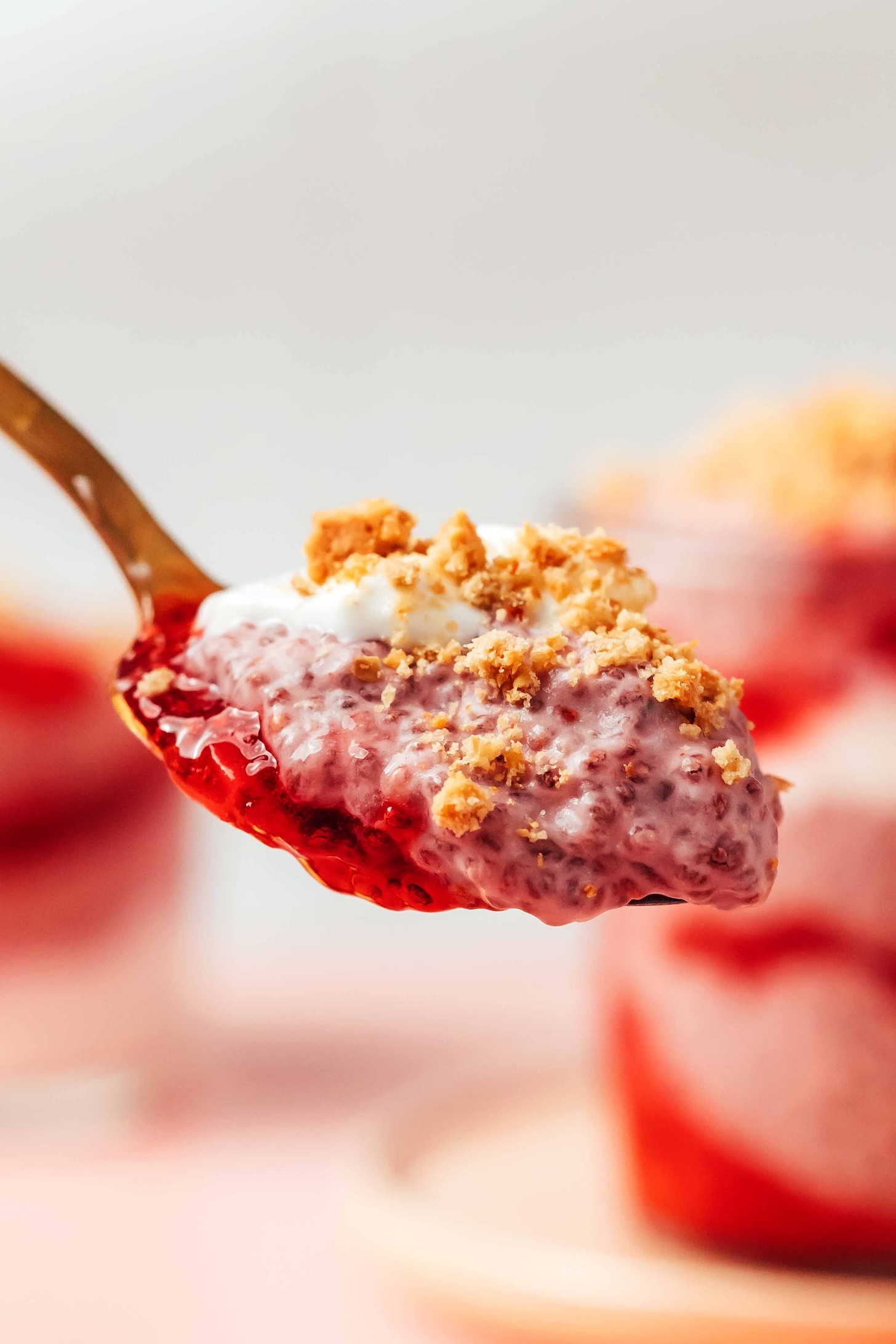 Spoonful of strawberry chia pudding with strawberry compote, yogurt, and crushed graham crackers