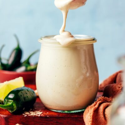 Vegan cashew dressing dripping from a spoon onto the rim of a jar filled with more dressing