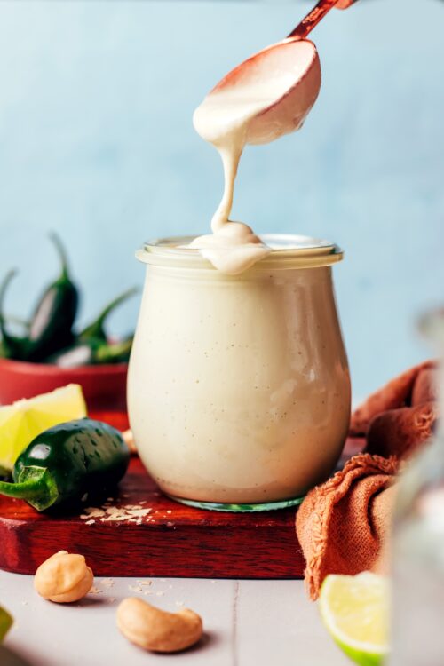 Vegan cashew dressing dripping from a spoon onto the rim of a jar filled with more dressing