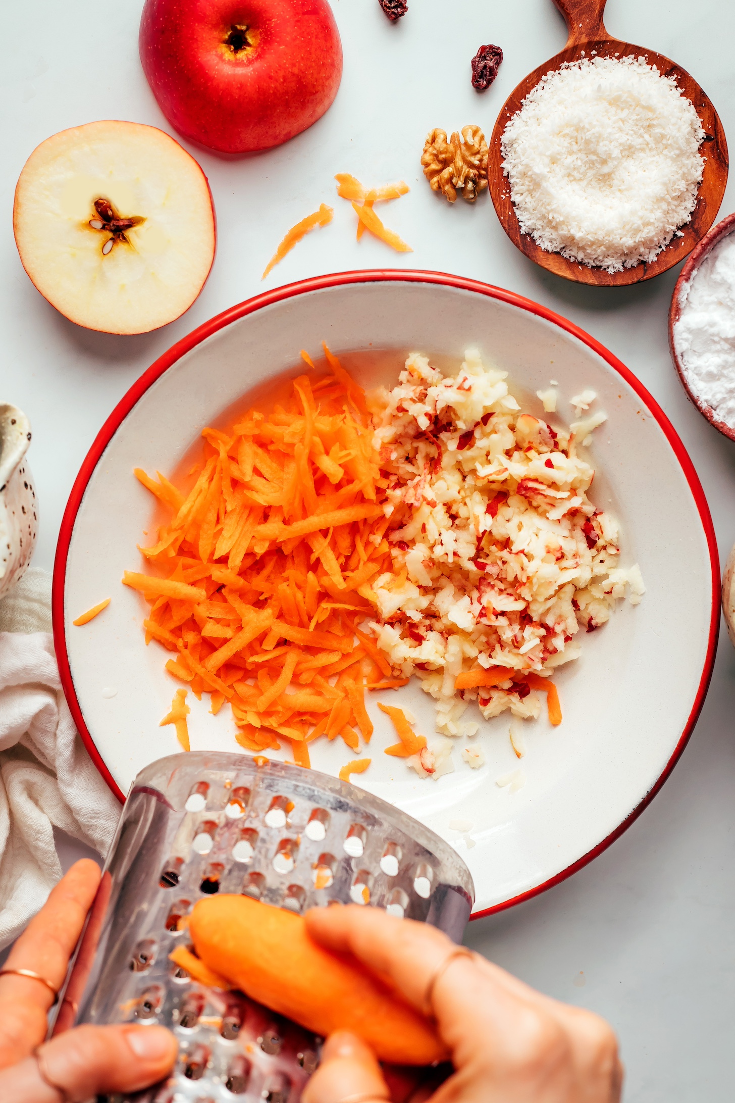 Grating carrot on a box grater into a bowl of grated carrot and apple