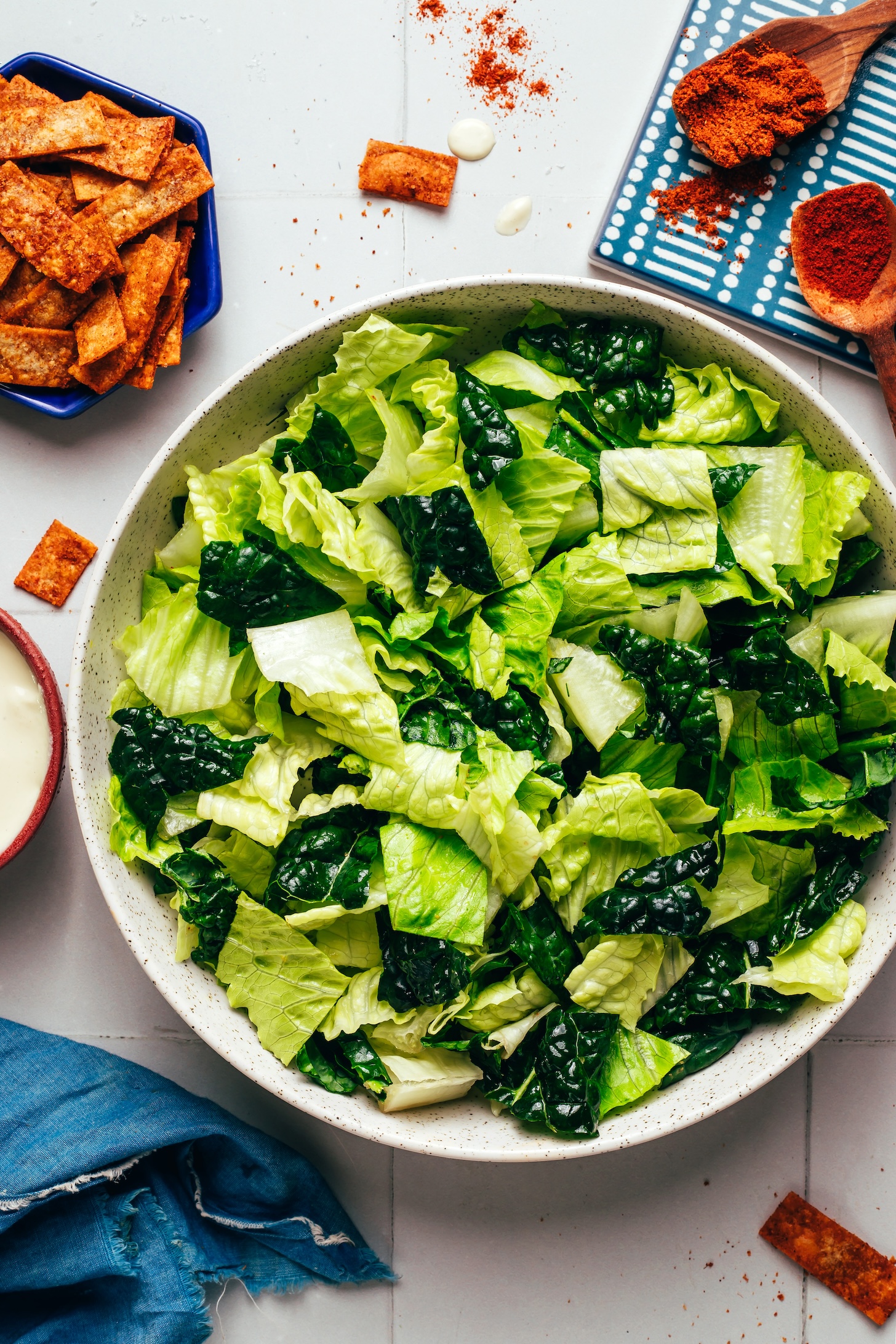 Bowl of chopped romaine and kale next to tortilla strips, dressing, and spices