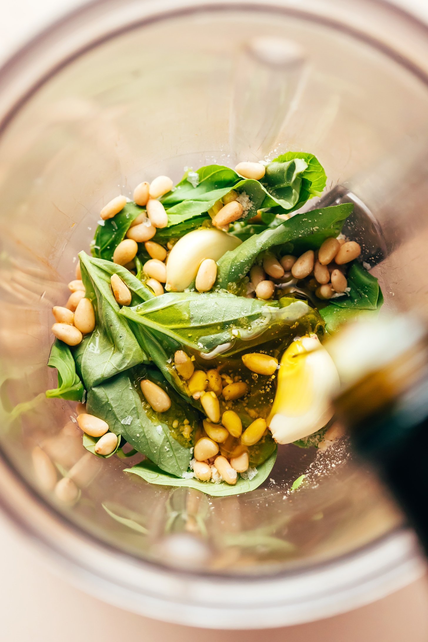 Drizzling olive oil into a blender with basil, pine nuts, garlic, and salt