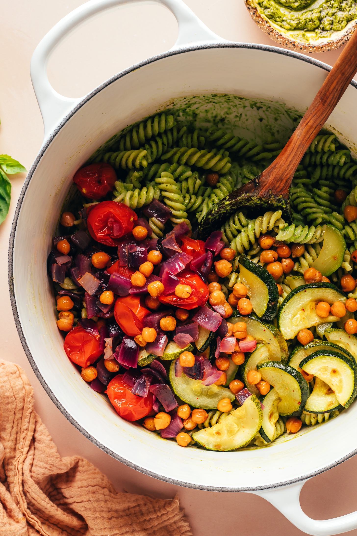 Freshly roasted zucchini, tomatoes, and red onion in a pot of pesto pasta