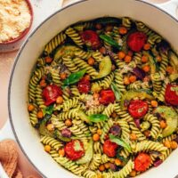 Dutch oven of zucchini pesto pasta with fresh basil, pesto, and vegan parmesan around it